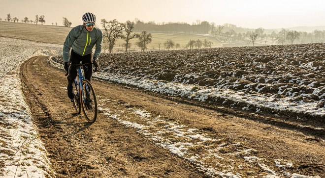 Mann auf Feldweg mit grauer Jacke.