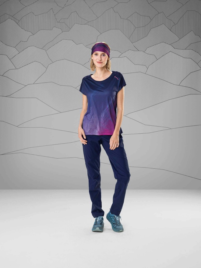 Frau mit violett-blauem T-Shirt und dunkelblauer Wanderhose vor grauem Hintergrund