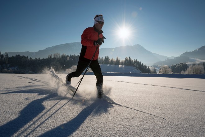 Mann mit roter Jacke fährt auf Langlaufski im Pulverschnee.