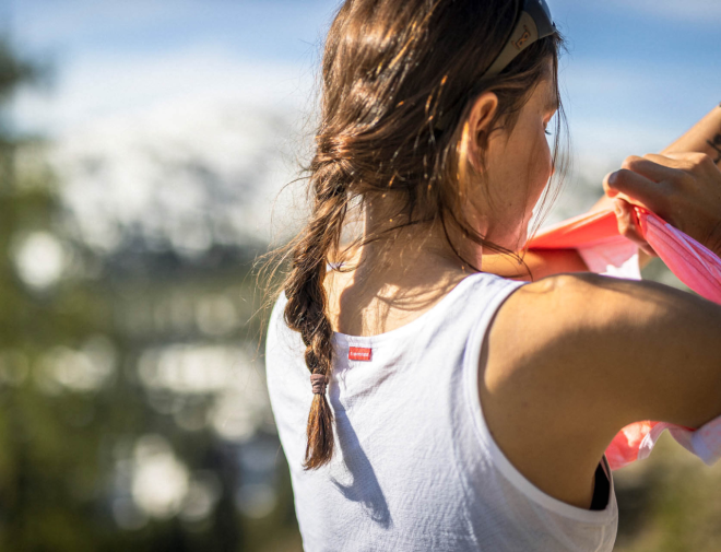 Woman in a white cycling singlet, putting on a road cycling jersey.