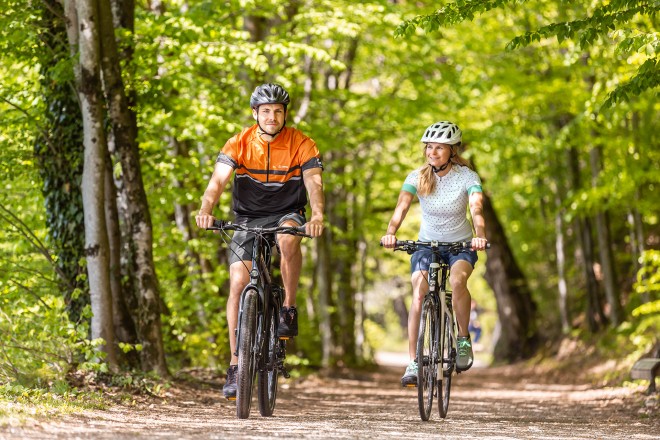 Man and woman riding on bikes through the forest in summer.